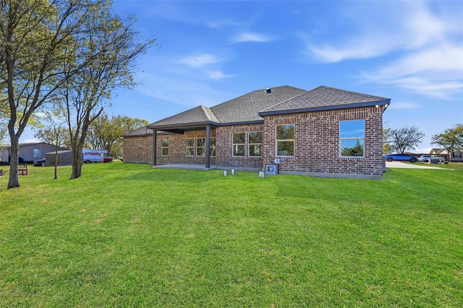 Back of property featuring brick siding, a patio area, roof with shingles, and a yard