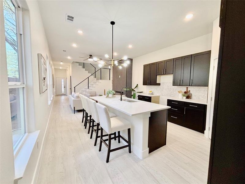 Kitchen with a breakfast bar, a center island with sink, hanging lights, light wood-style flooring, and dark wood finish cabinets