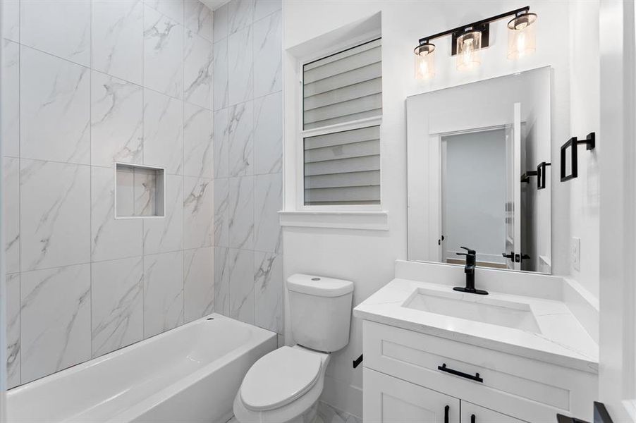 This modern bathroom features sleek white marble tile, a tub with built-in shelving, a stylish vanity with a black faucet, and contemporary lighting.