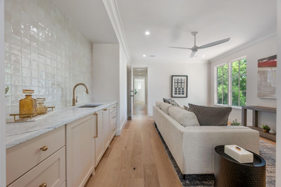 An open living space features custom wet bar cabinetry, stone countertops, and warm hardwood flooring.