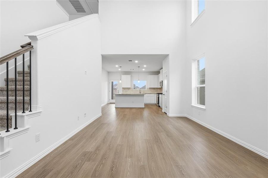 Unfurnished living room featuring healthy amount of natural light, light wood-style floors, stairs, and a towering ceiling