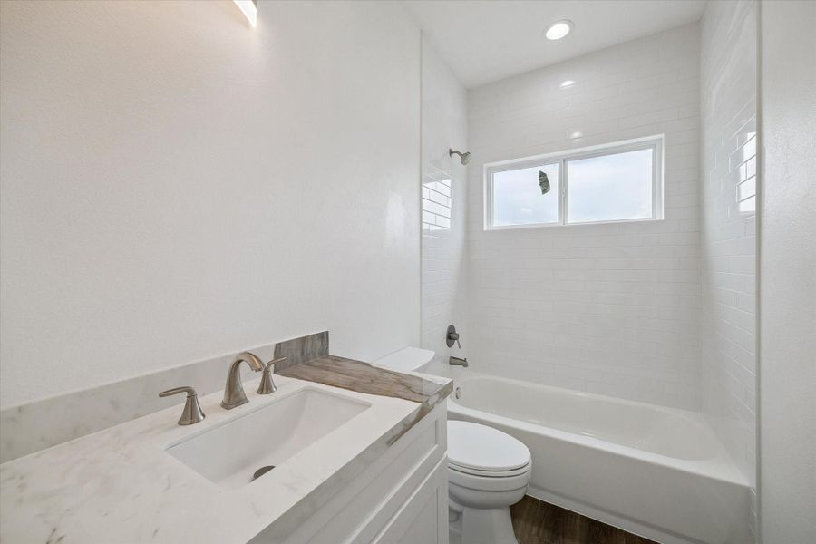 Bright and beautifully finished, this full bathroom pairs a white vanity with elegant stone-look countertops, brushed-metal fixtures, and a clean undermount sink. The tub and shower combination is surrounded by glossy white subway tile for a timeless, polished look. A wide window brings natural light into the space, while recessed lighting keeps the room bright and inviting. Warm flooring adds contrast and continuity with the home’s contemporary interior design. Bright and beautifully finished, this full bathroom pairs a white vanity with elegant stone-look countertops, brushed-metal fixtures, and a clean undermount sink. The tub and shower combination is surrounded by glossy white subway tile for a timeless, polished look. A wide window brings natural light into the space, while recessed lighting keeps the room bright and inviting. Warm flooring adds contrast and continuity with the home’s contemporary interior design.