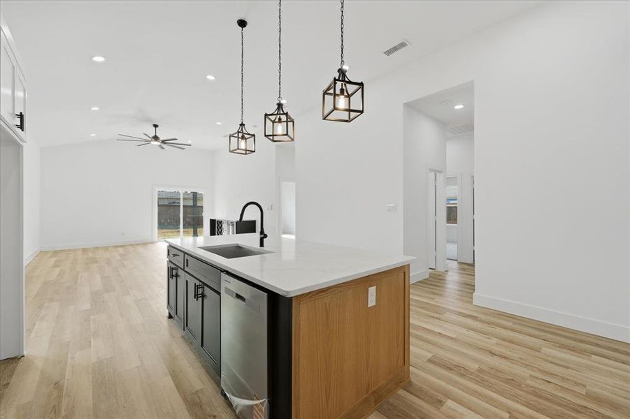 Kitchen with open floor plan, vaulted ceiling, a kitchen island with sink, light wood-type flooring, and dishwasher