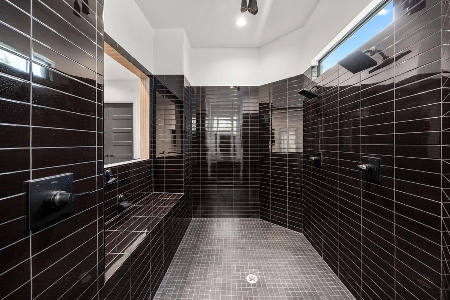 This is a spacious, modern shower with sleek dark tiles, dual showerheads, and a built-in bench, offering a luxurious and contemporary feel.