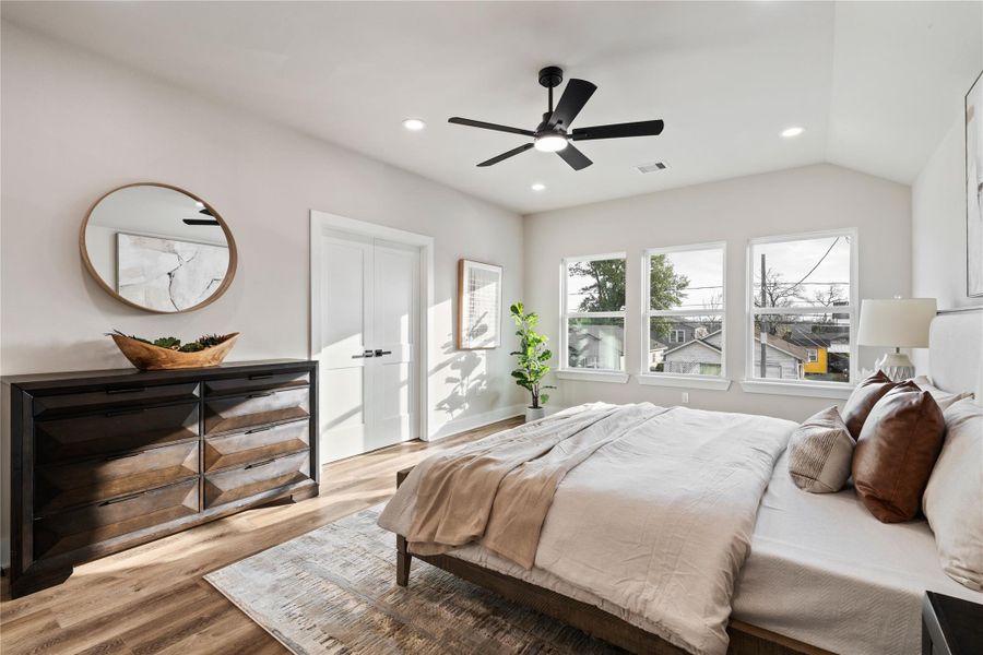 This serene bedroom offers a bright, spacious atmosphere with an elevated ceiling and wide windows that frame the neighborhood view. It’s a relaxing escape designed to feel comfortable, open, and effortlessly welcoming.