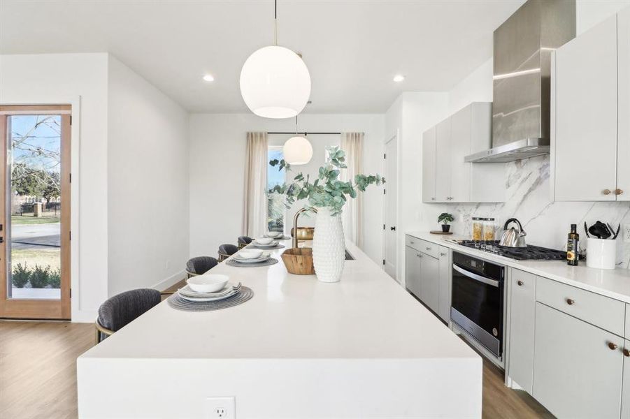 Kitchen featuring pendant lighting, a center island, wall chimney exhaust hood, stainless steel gas cooktop, and oven