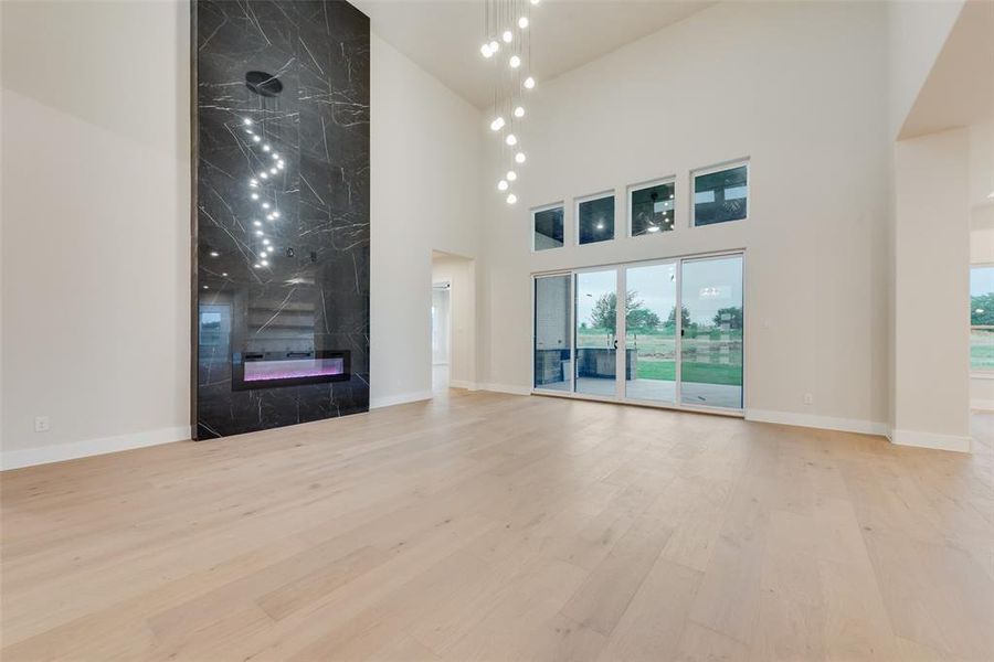 Unfurnished living room with a towering ceiling, plenty of natural light, wood finished floors, and baseboards Unfurnished living room with a towering ceiling, plenty of natural light, wood finished floors, and baseboards