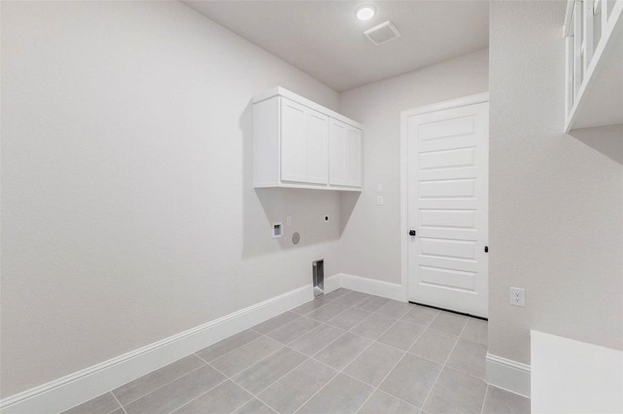 Spacious laundry room with tile flooring, white cabinetry, and utility hookups.