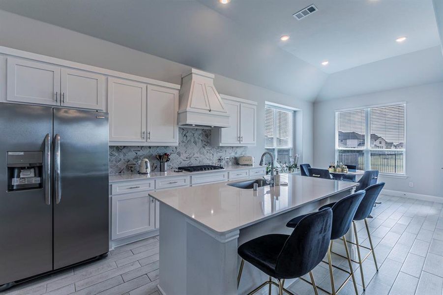 Kitchen with stainless steel built in refrigerator, wood finish floors, backsplash, light stone countertops, and lofted ceiling Kitchen with stainless steel built in refrigerator, wood finish floors, backsplash, light stone countertops, and lofted ceiling