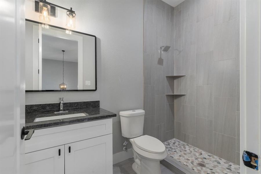 Bathroom with toilet, tiled shower, vanity, and baseboards