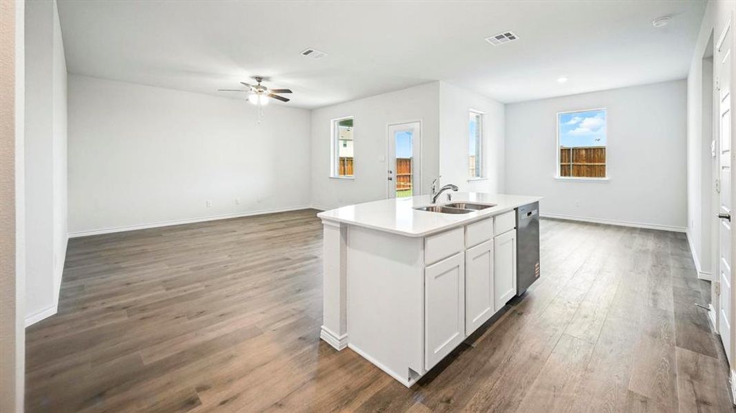 Open-concept living space featuring wood-finish flooring, a contemporary ceiling fan, and multiple windows providing natural light