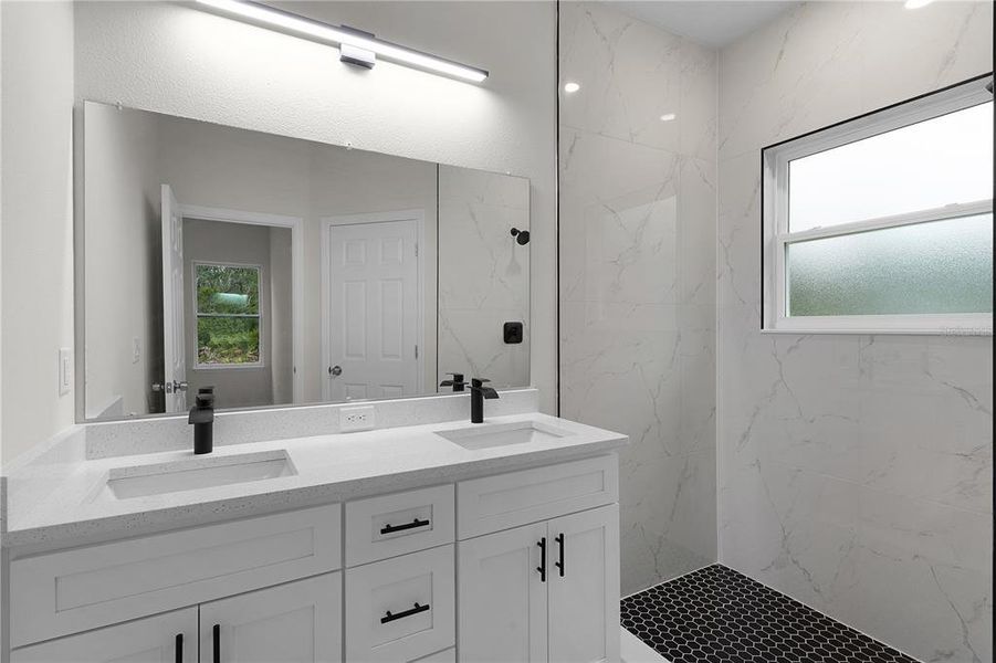 Double sinks and tiled shower in primary bathroom. The closed door to the separate toilet room is visible in the mirror.