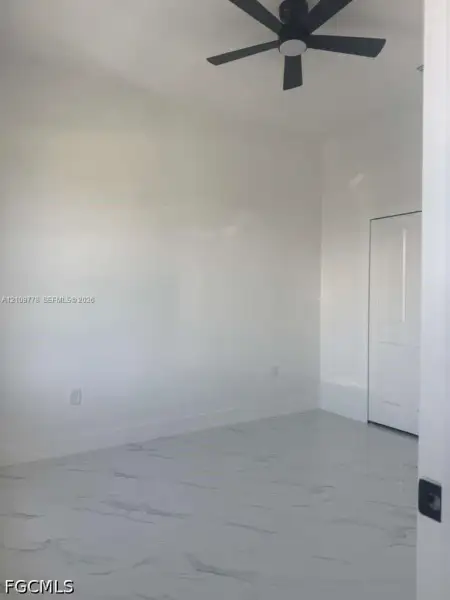Interior space featuring large-format tile flooring with a neutral veined pattern, crisp white walls, and a matte black ceiling fan Interior space featuring large-format tile flooring with a neutral veined pattern, crisp white walls, and a matte black ceiling fan