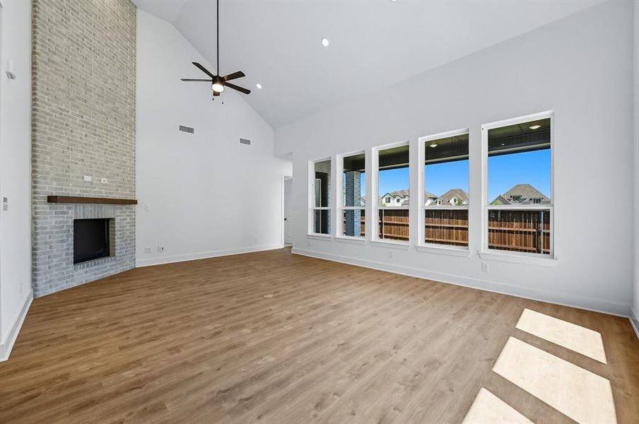 Unfurnished living room with a brick fireplace, high vaulted ceiling, light wood-style flooring, ceiling fan, and recessed lighting Unfurnished living room with a brick fireplace, high vaulted ceiling, light wood-style flooring, ceiling fan, and recessed lighting