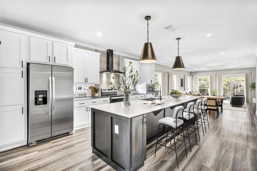 Kitchen with stainless steel appliances, white cabinets, a breakfast bar area, a large island, and wall chimney exhaust hood