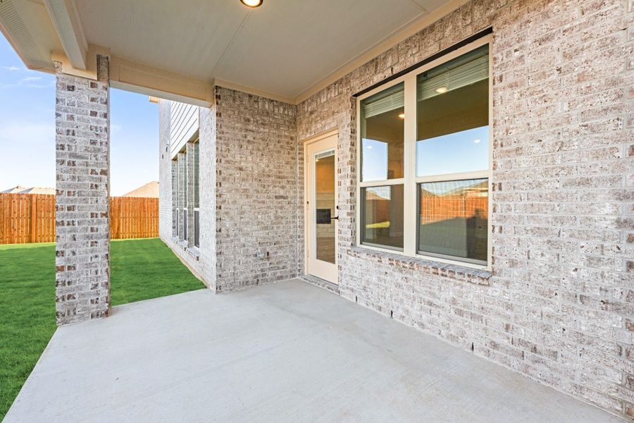 Covered back patio with concrete floor, light brick exterior, and fenced backyard with green lawn Covered back patio with concrete floor, light brick exterior, and fenced backyard with green lawn