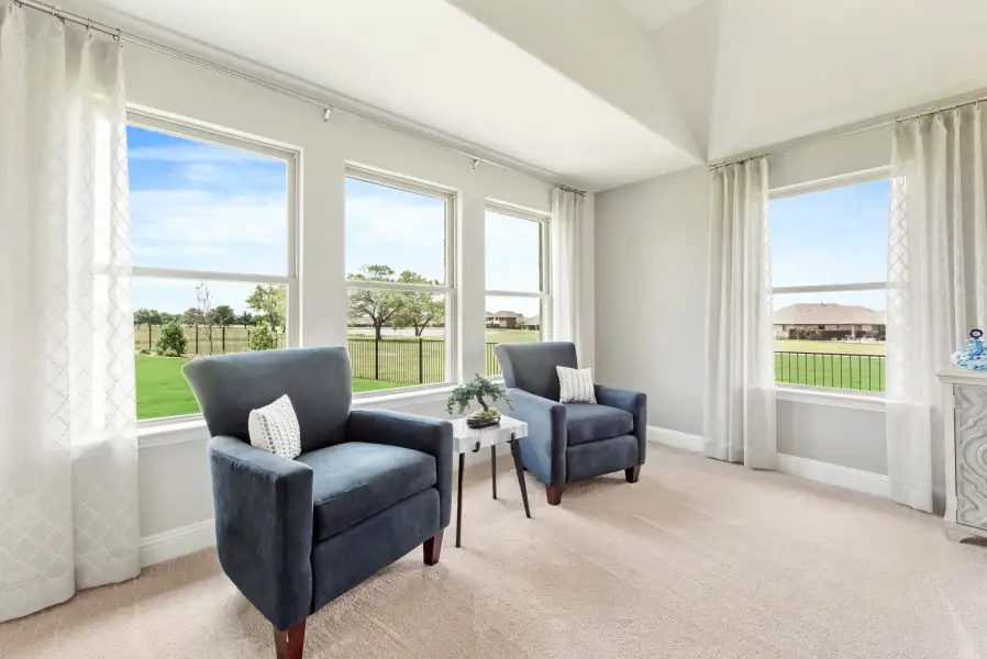 Sitting area with two blue armchairs, carpet flooring, and large windows overlooking a backyard