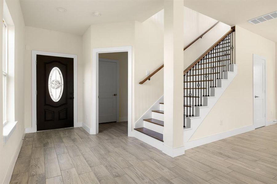 Upon entering you find and inviting entryway featuring wood-like floors, fresh paint, and a beautifully designed staircase, creating a warm and welcoming atmosphere as you step into the home.