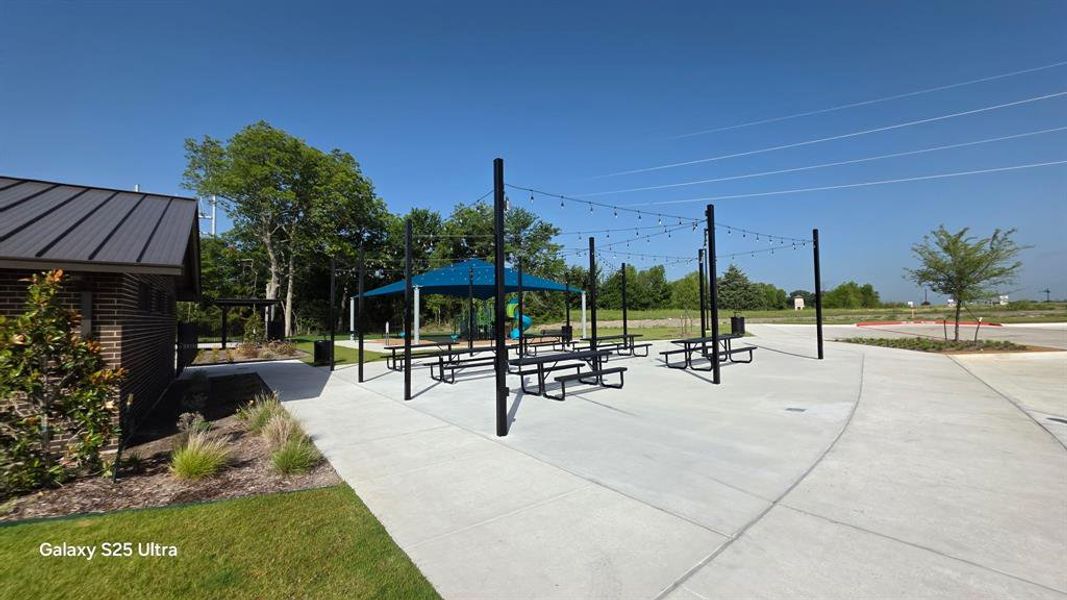 Outdoor gathering area featuring multiple picnic tables, strung lighting, and a shaded canopy Outdoor gathering area featuring multiple picnic tables, strung lighting, and a shaded canopy
