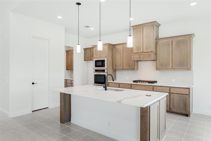 Kitchen with large quartz island, tan wood cabinets, stainless double ovens, and pendant lights over tile floors