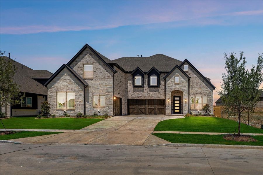 Two-story stone home with three-car garage, arched entry, and manicured front lawn at dusk