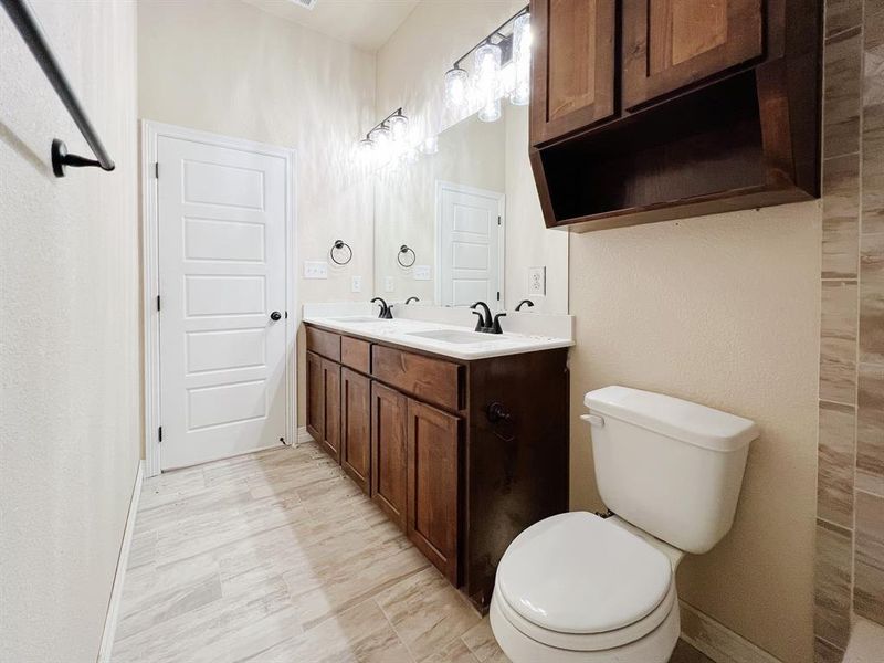 Bathroom featuring double vanity and a textured wall Bathroom featuring double vanity and a textured wall