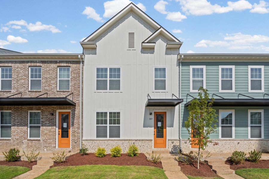 White vertical siding, brick facade, and blue horizontal siding exteriors with contrasting wood-finish entry doors and black awnings White vertical siding, brick facade, and blue horizontal siding exteriors with contrasting wood-finish entry doors and black awnings