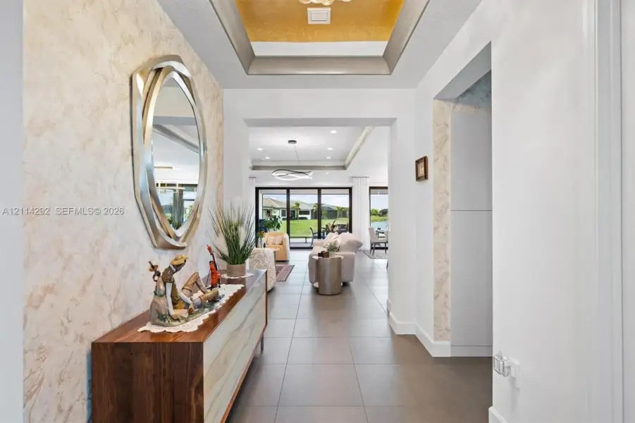 Foyer featuring a recessed tray ceiling with metallic finish, textured wall detailing, and large-format tile flooring