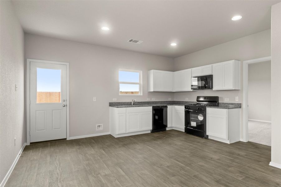 Kitchen featuring black appliances, white cabinets, wood finished floors, and recessed lighting