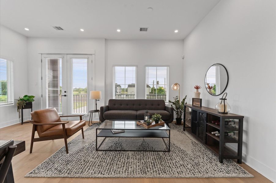 Perched on the second floor, this open-concept living, dining, and kitchen area flows effortlessly beneath high ceilings and across rich engineered hardwood floors that unify the space with warmth and elegance. A set of French doors anchors the room, inviting natural light and offering a glimpse of downtown through the balcony beyond. The layout encourages seamless entertaining and everyday comfort, with each zone connected yet distinct, framed by clean lines and contemporary finishes.