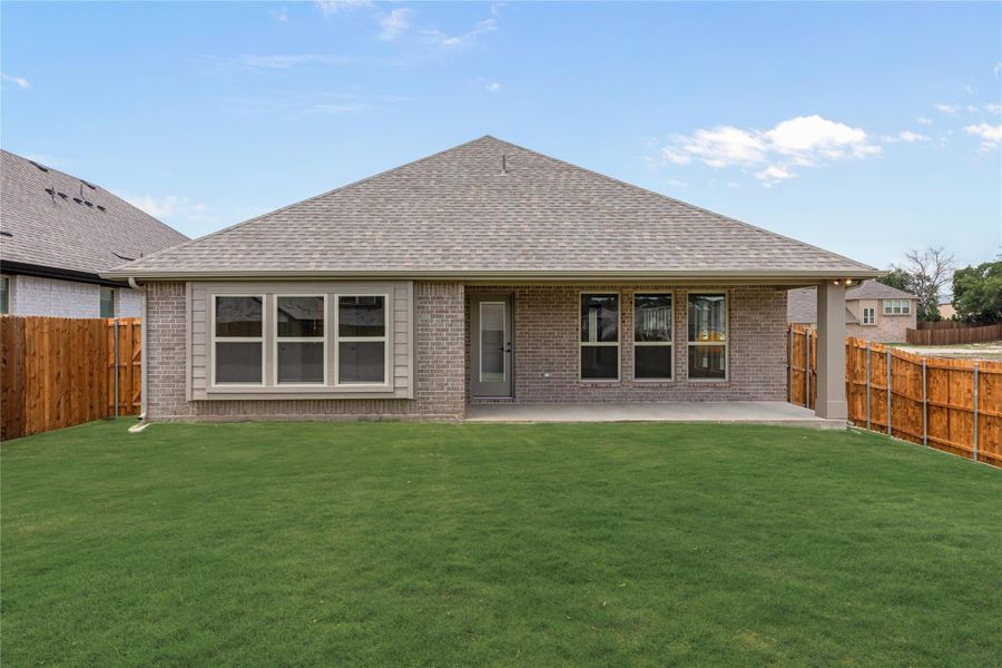 Rear exterior of brick home with covered patio, large green lawn, and wood privacy fence Rear exterior of brick home with covered patio, large green lawn, and wood privacy fence