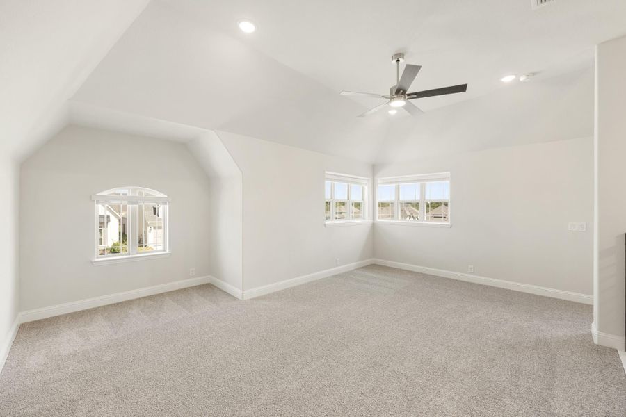 Empty bedroom with vaulted ceiling, ceiling fan, carpet flooring, and two windows