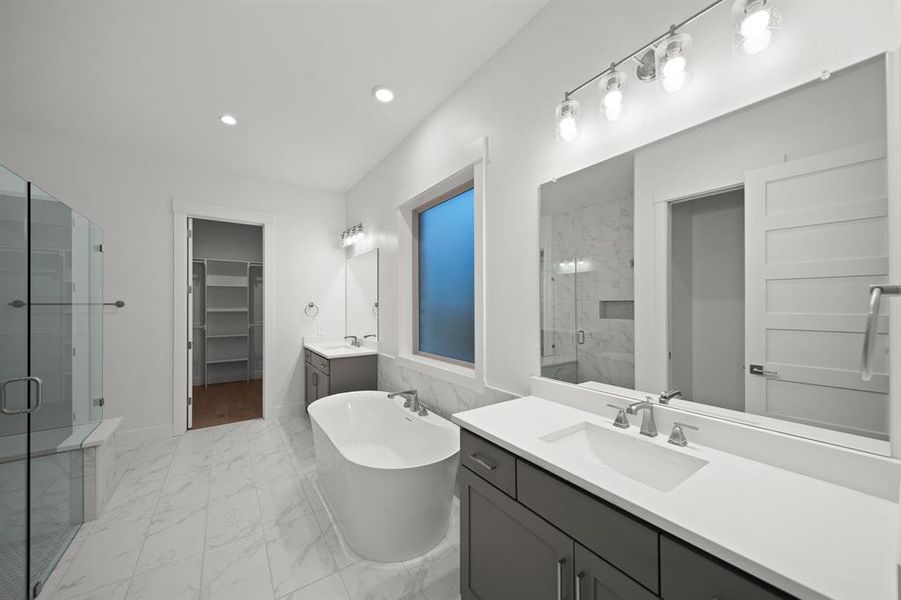 Bathroom with a spacious closet, two vanities, a marble finish shower, light marble finish floors, and a soaking tub