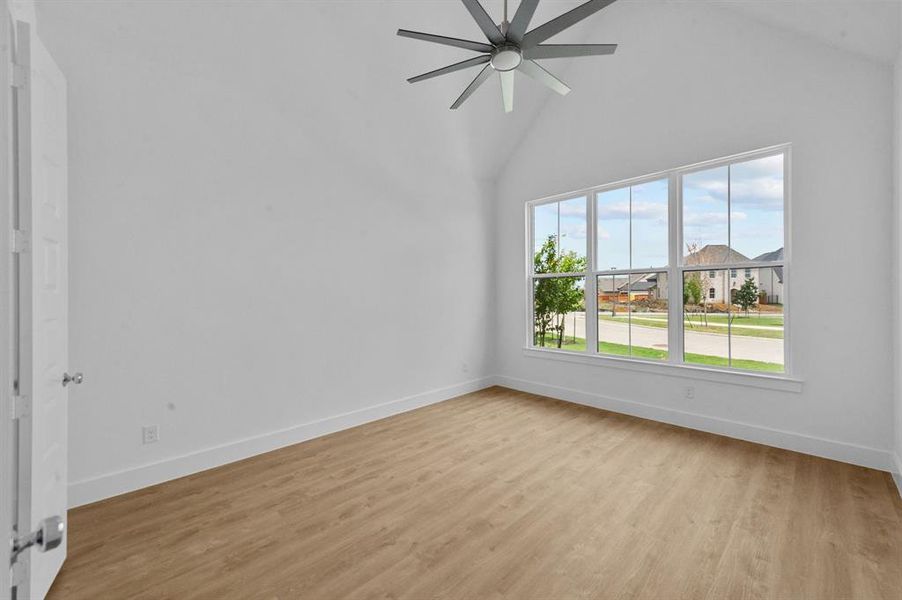 Empty room with light wood-style floors, high vaulted ceiling, baseboards, and a ceiling fan