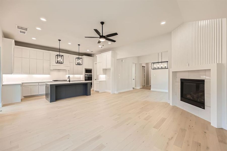 Kitchen featuring white cabinetry, appliances with stainless steel finishes, hanging light fixtures, an island with sink, and light hardwood / wood-style floors