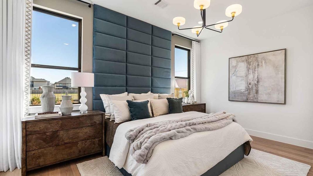 The primary bedroom with ceiling fan, three large windows for natural lighting, hardwood floors, and a large walk-in closet.