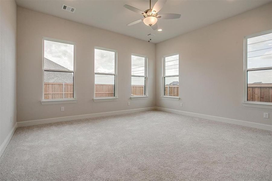 Unfurnished room featuring ceiling fan, light colored carpet, and a healthy amount of sunlight