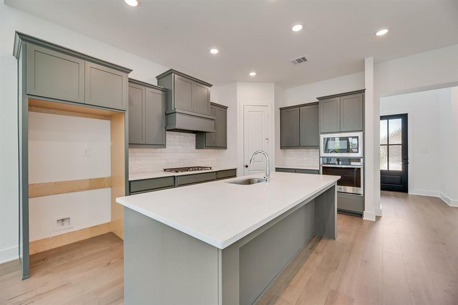 Kitchen with backsplash, a center island with sink, stainless steel appliances, light wood finished floors, and recessed lighting Kitchen with backsplash, a center island with sink, stainless steel appliances, light wood finished floors, and recessed lighting
