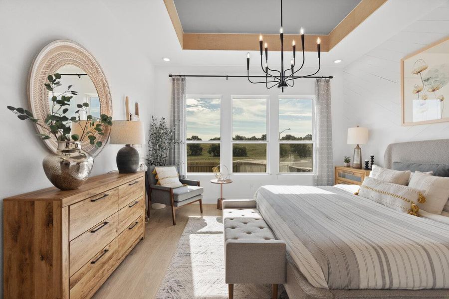 Bedroom with a raised ceiling, light wood-type flooring, and suspended lighting