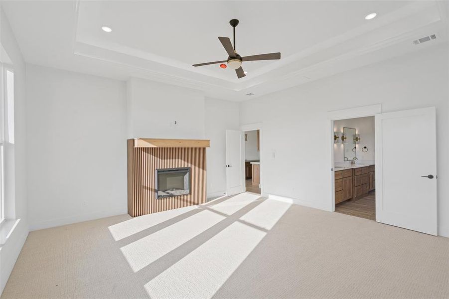 Unfurnished bedroom featuring ensuite bath, light colored carpet, a raised ceiling, ceiling fan, and sink