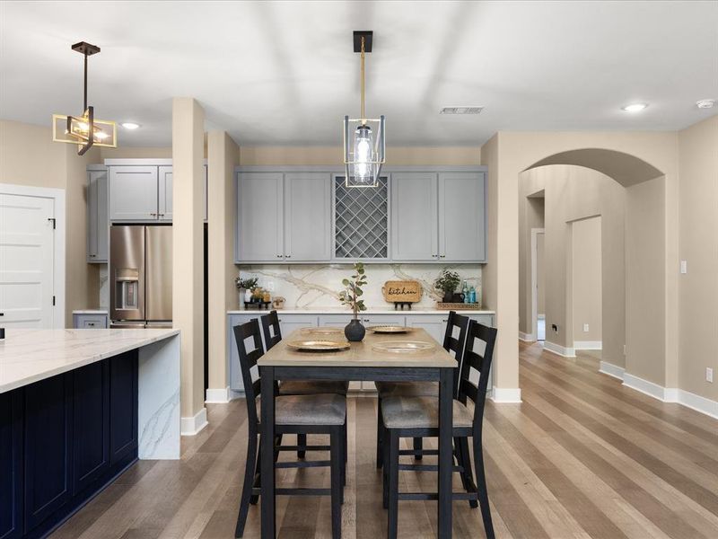 Kitchen with arched walkways, gray cabinets, light stone counters, pendant lighting, and light wood finished floors