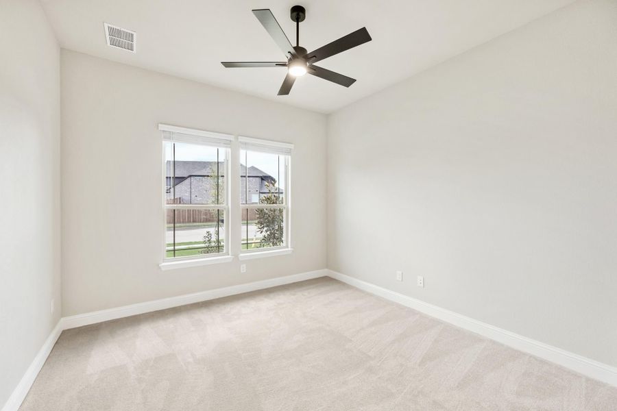 Empty bedroom with beige carpet, black ceiling fan, and double window with neighborhood view