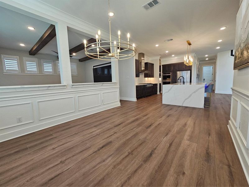 This photo showcases a modern open-concept kitchen and dining area with elegant wood flooring, a large island with a marble countertop, and stylish pendant lighting. The room features dark cabinetry, stainless steel appliances, and decorative ceiling beams, creating a warm and inviting atmosphere. This photo showcases a modern open-concept kitchen and dining area with elegant wood flooring, a large island with a marble countertop, and stylish pendant lighting. The room features dark cabinetry, stainless steel appliances, and decorative ceiling beams, creating a warm and inviting atmosphere.