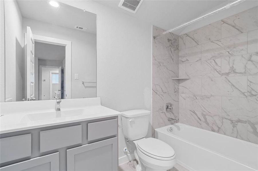 Secondary bath features tile flooring, bath/shower combo with tile surround, stained wood cabinets, beautiful light countertops, mirror, sleek fixtures and modern finishes.