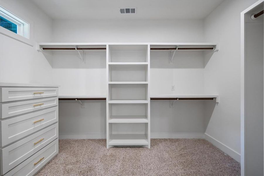 Spacious closet featuring light colored carpet, built in cabinets and shelving