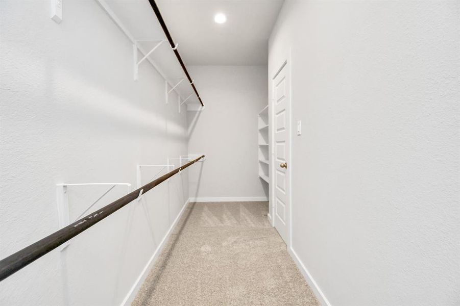 Walk-in closet that epitomizes luxury and practicality. This generously sized space features built-in shelving, offering abundant room for impeccable organization. High ceilings and recessed lighting create a bright and welcoming ambiance. Example photo of completed home with similar plan. Actual may vary.