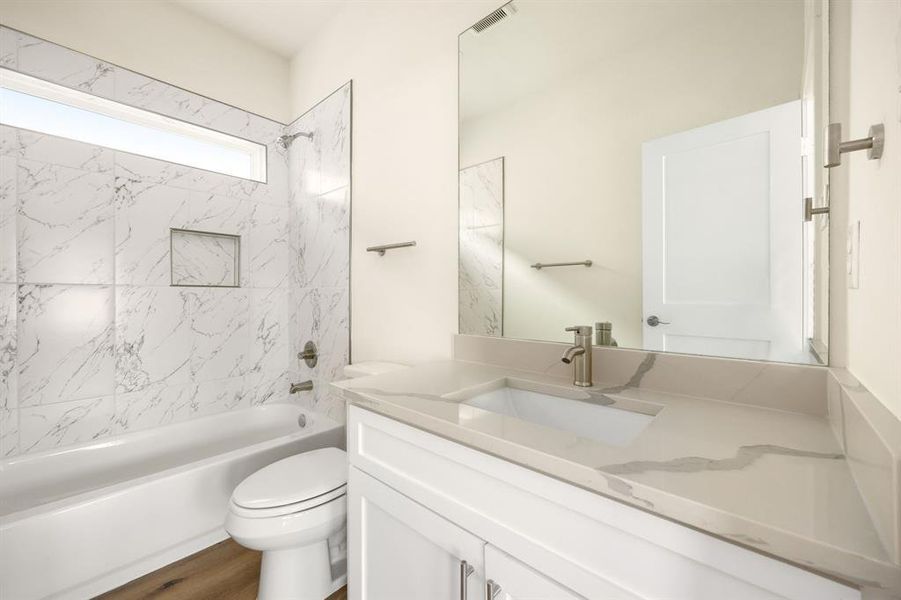 Secondary bathroom features light countertops and cabinets, custom paint, shower/tub combo with tile surround, large mirror, tile floors, sleek fixtures and modern finishes, plenty of space to accommodate any visiting family or guests.