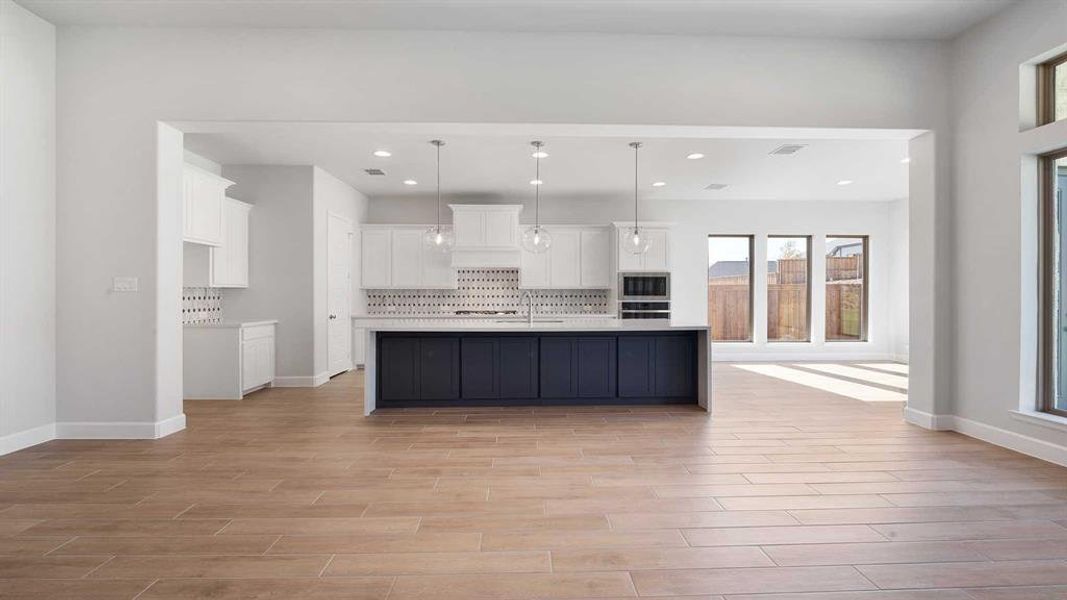 Kitchen with white cabinets, light wood-type flooring, pendant lighting, and an island with sink