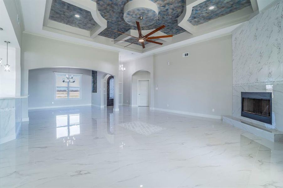 Unfurnished living room with ceiling fan, a high end fireplace, light marble finish flooring, a chandelier, and a towering ceiling