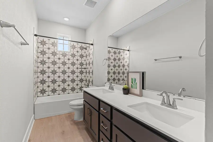 Bathroom featuring light wood-style floors, shower / bathtub combination with curtain, double vanity, and a textured wall Bathroom featuring light wood-style floors, shower / bathtub combination with curtain, double vanity, and a textured wall